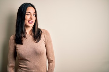 Obraz premium Young brunette woman with blue eyes wearing casual sweater over isolated white background winking looking at the camera with sexy expression, cheerful and happy face.