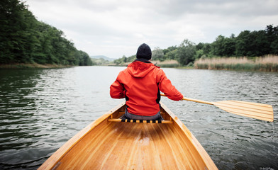 Rear view of man in red jacket paddling canoe on cloudy day