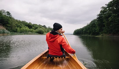 Foto op Canvas Bearded man paddling canoe on cloudy day. Canoeing on rainy day © yossarian6
