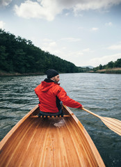 Rear view of man in red jacket paddling canoe on cloudy day