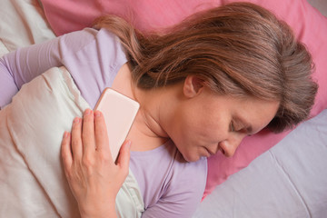 Woman sleeps with mobile phone in a bed. Middle aged 40 years woman lying on pillow and holds...