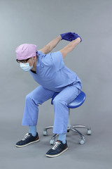 Dentist in uniform and mask and eyeglasses , stretching arms in studio - healthy lifestyle at work...