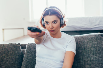 attractive girl in headphones holding remote controller and watching tv at home during self isolation