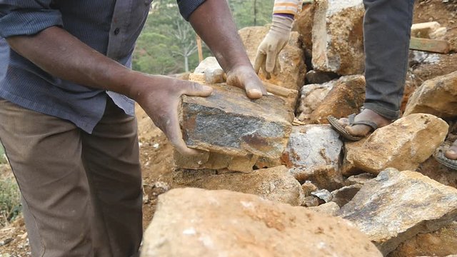 Male hands of indian stonemason puts a block of stone for builds flowerbed. Adult unrecognizable stone worker creates new construction in botanical garden. Close up Slow motion