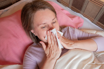 Woman sneezes, has a running nose or seasonal allergy. Middle aged 40 years woman lying in the bed...
