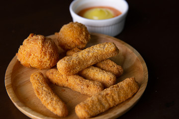 Nuggets and Cheese Balls on a wooden plate on a black background