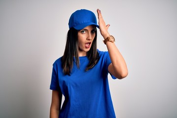 Young delivery woman with blue eyes wearing cap standing over blue background surprised with hand on head for mistake, remember error. Forgot, bad memory concept.