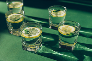 Five glasses of water with lemon slices on green background. Selective focus