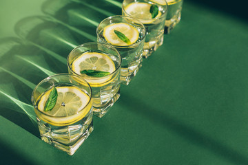 Glasses of water with lemon and mint on green background. Refreshing healthy summer drink....