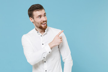 Excited young bearded man guy 20s in white classic shirt isolated on pastel blue wall background studio portrait. People emotions lifestyle concept. Mock up copy space. Pointing index finger aside up.