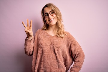 Young beautiful blonde woman wearing casual sweater and glasses over pink background showing and...