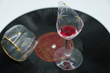 &nbsp; Broken vintage wine glass with red wine on an old vinyl record. Still life in art deco style.