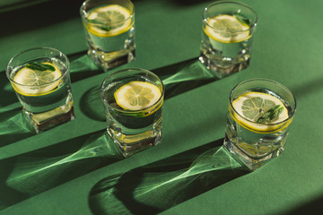 Fresh tonic drinks. Glasses of water with lemon slices and mint leaves on green background. Summer...