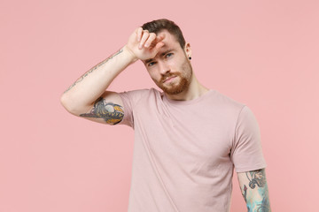 Exhausted tired young bearded tattooed man guy in pastel casual t-shirt posing isolated on pink background studio portrait. People emotions lifestyle concept. Mock up copy space. Put hands on head.