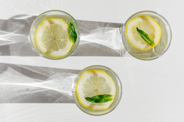 Top view of three glasses with fresh lemonade on white wooden background. Refreshing and tonic...