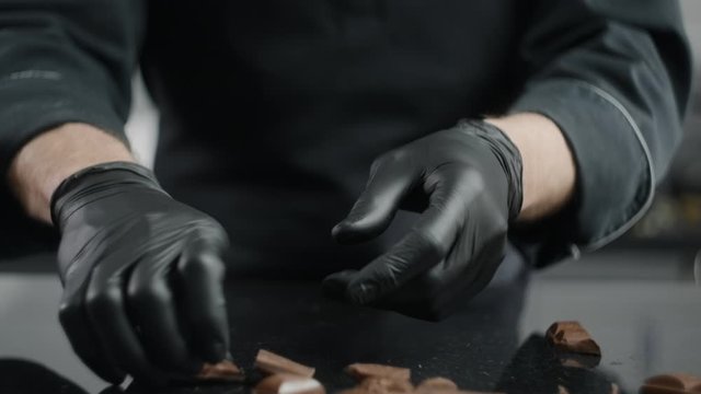 Chef chocolatier breaks chocolate bar to the small pieces for melting and making sweets, raw materials for making sweets and chocolate, cooking the sweet desserts, making chocolate, Full HD 240fps