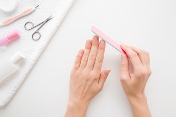 Young woman hands using nail file. Simple manicure set on white towel. Light gray table background. Closeup. Point of view shot. Top down view.