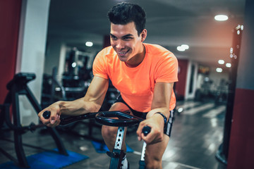 Fototapeta na wymiar Man biking in the gym, exercising legs doing cardio workout cycling bikes.