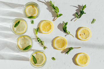 Cold fresh lemonade on white wet wooden background. Healthy tonic drink. Water with lemon and mint...