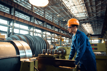 Male worker checks turning lathe on plant