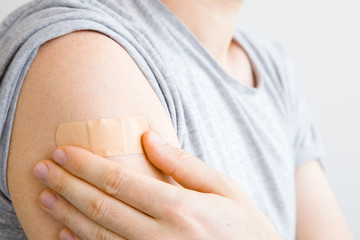 Young man hand putting brown adhesive bandage on his arm after scratch on skin. First aid. Self help. Healthcare concept. Closeup.