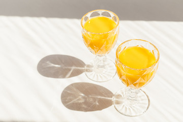 Two beautiful faceted glasses of fresh squeezed orange juice on white wooden table. Citrus drink in wineglass, vitamin C