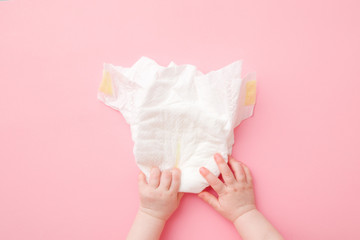 Baby hands touching white diaper on light pink table background. Pastel color. Closeup. Point of view shot. Top down view.