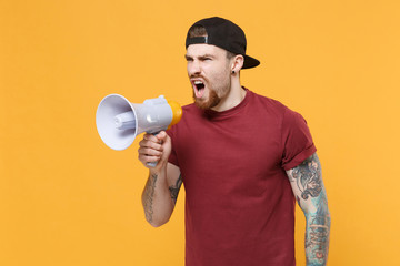 Angry irritated young bearded tattooed man guy in casual t-shirt black cap isolated on yellow background in studio. People lifestyle concept. Mock up copy space. Screaming in megaphone looking aside.