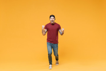 Fototapeta na wymiar Happy young bearded tattooed man guy in casual t-shirt black cap posing isolated on yellow background in studio. People emotions lifestyle concept. Mock up copy space. Clenching fists like winner.