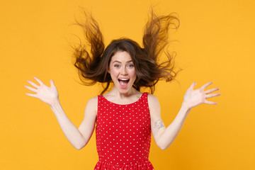 Excited young brunette woman girl in red summer dress posing isolated on yellow wall background studio portrait. People lifestyle concept. Mock up copy space. Spreading hands, throwing flying hair.