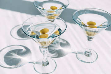Fresh home made vodka martini with olives in cocktail glasses on white background with shadows.