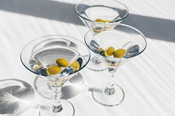 Home made dry martini in cocktail glasses with olives on white background with sun lighting shadows. Close-up