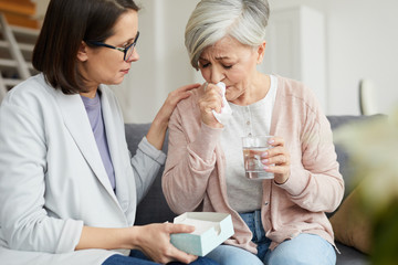 Portrait of adult female psychologist helping crying senior woman during therapy session in office