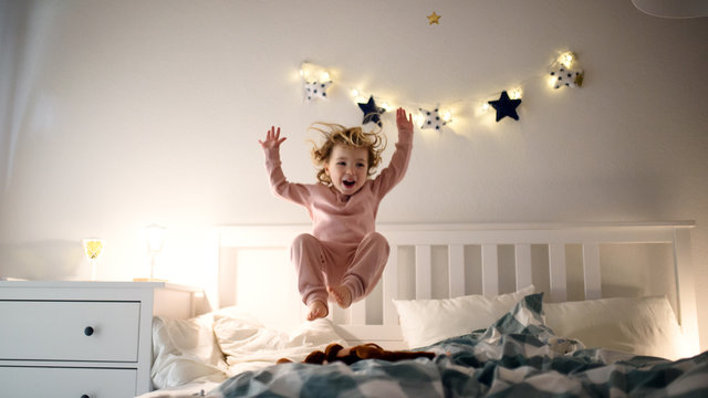 Two small children jumping on bed indoors at home, having fun.