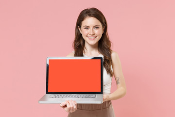 Naklejka premium Smiling young brunette woman girl in light casual clothes posing isolated on pastel pink wall background. People lifestyle concept. Mock up copy space. Hold laptop pc computer with blank empty screen.