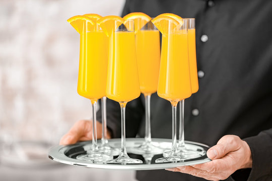Waiter with glasses of tasty mimosa cocktail at banquet