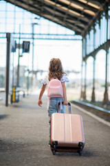 Child walks with her backpack and suitcase by the station