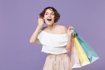 Curious young woman girl in summer clothes hold package bag with purchases isolated on pastel...