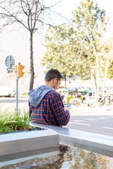 Rear view of a fashion cool urban bearded male with smartphone on city street.