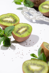 selective focus of green kiwi fruits near peppermint and black seeds on white