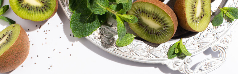 horizontal concept of tasty kiwi fruits near fresh peppermint on silver plate on white