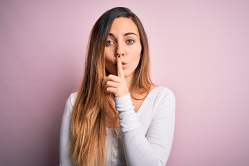 Young beautiful blonde woman with blue eyes wearing white t-shirt over pink background asking to be quiet with finger on lips. Silence and secret concept.
