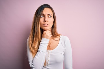 Fototapeta premium Young beautiful blonde woman with blue eyes wearing white t-shirt over pink background Touching painful neck, sore throat for flu, clod and infection