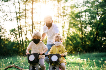 Father with two small children and face masks on cycling trip in nature.