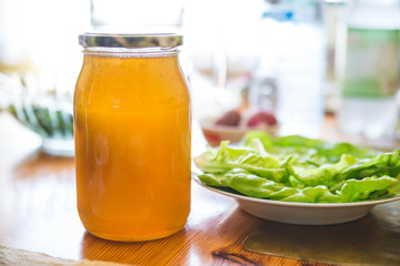 Jar of golden honey without label on wooden table in the kitchen next to cut lettuce. Bright food background
