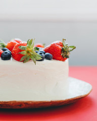 Cut view of beautiful summer cake decorated with strawberries and blueberries on red table