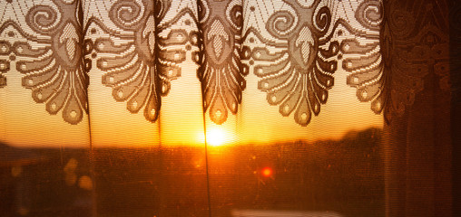 Golden sunset background visible through patterned curtains and balcony glass door