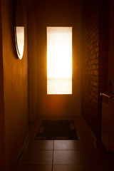Warm sunset light visible in the corridor through old patterned doors with smooth light reflection in the mirror and brick wall