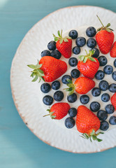 A tasty appetizing celebratory summer sponge cake with whipped cream, blueberry and strawberry on blue table background. Top view