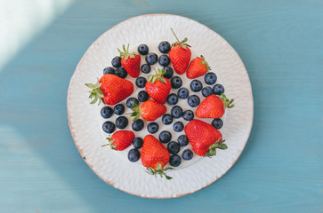 Top view od delicious celebratory summer cake with white cream and berries on blue table background. Bluberry and strawberry